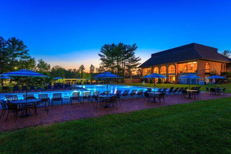 In-ground L shaped pool surrounded with brick patios. Variety of tables, umbrellas, & chairs.